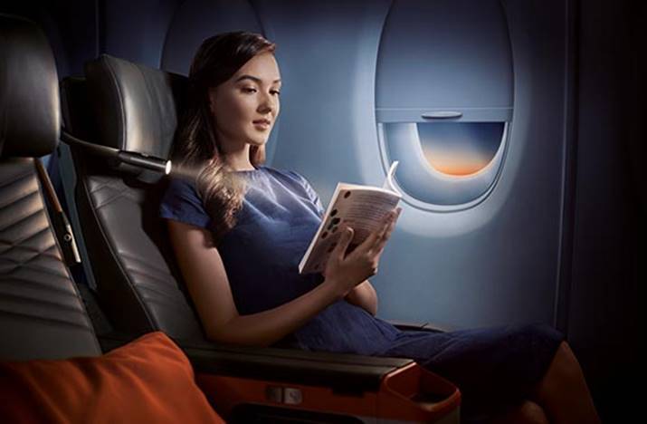 woman with long dark hair reading a book on a singapore airlines a350